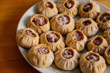 Steamed national Mongolian food dumpling Buuz filled with minced beef, white plate, wooden table, Close up east Siberian Buryats dish poses, Juicy minced meat wrapped handmade dough shirt buuza