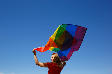 girl with lgbt flag behind her back against a bright blue sky