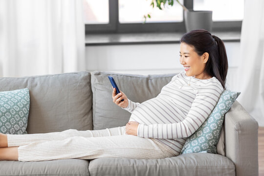 pregnancy, rest, people and expectation concept - happy smiling pregnant asian woman with smartphone sitting on sofa at home - Powered by Adobe