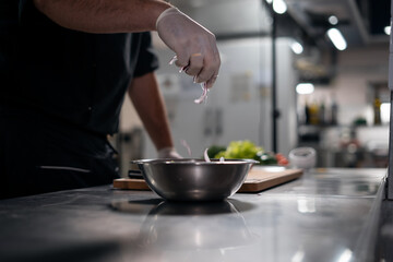 chef cook hands in gloves prepare salad and adding red onion in bowl at kitchen