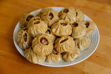 Steamed national Mongolian food dumpling Buuz filled with minced beef, white plate, wooden table, Close up east Siberian Buryats dish poses, Juicy minced meat wrapped handmade dough shirt above view