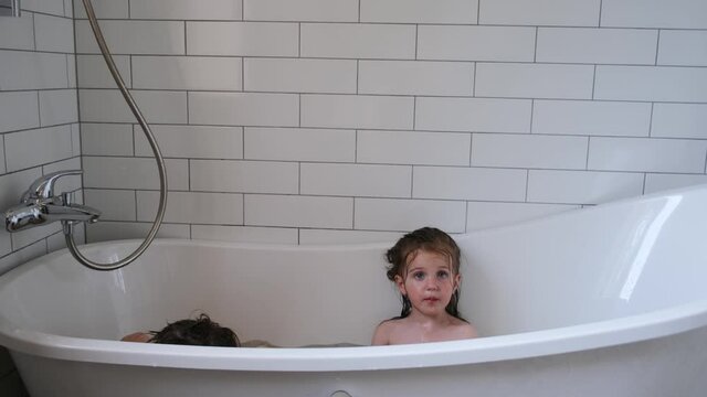 Adorable little children siblings sit in large comfortable bathtub near decorated with tiles wall in spacious bathroom at home
