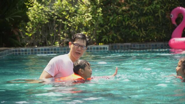 Happy asian family with inflatable or life jacket playing in swimming pool at hotel enjoying summer vacation. young father and  daughter and son relaxing in swimming pool together outdoors