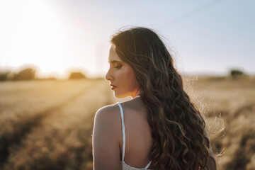 Gorgeous Spanish woman with long blond hair looking down in a wheat field under the sun