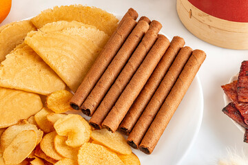 Chocolate wafer rolls in Chinese New Year snack platter alongside kuih kapit or Chinese Love Letters; arrowhead chips or fried ngaku chips; pork jerky or bakkwa; and mandarin oranges.