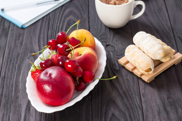 Fresh organic summer berries and fruits in a white plate on a black background.