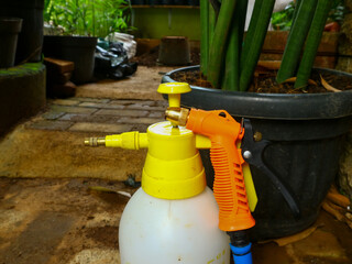 Closeup of a hand sprayer with a yellow cap and a sprinkler in a garden