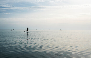 Young man floating on stand up paddle board on the sea on sunny summer day, active lifestyle, outdoor activity
