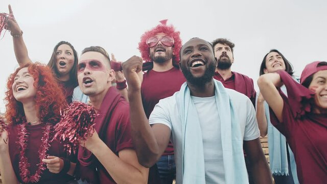 Group of multiracial sport supporters fans in red and blue having fun during football league world game and celebrating a goal and victory