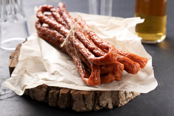 Closeup of delicious long dry sausages on the paper and wooden boar,bottle of beer and glasses on the background