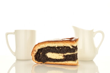 One fragrant freshly baked poppy roll slice with white ceramic cup and milk jug, close-up, isolated on white.