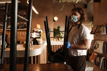 Young white cafe employee in face mask working indoors