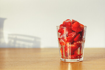 Ready to eat cut strawberries sprinkled with sugar in a glass. Summer law sugar dessert on wooden kitchen table. Soft selective focus.