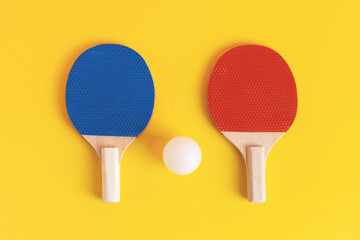 A pair of blue and red table tennis rackets with white ball on yellow background. Table tennis or...