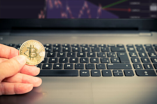 mano che tiene una moneta Bitcoin dorata su un computer portatile per analizzare il mercato delle criptovalute. Criptovaluta BTC. Valuta digitale.