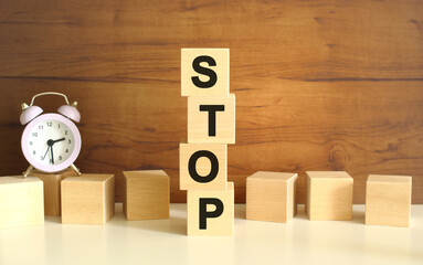 Four wooden cubes stacked vertically on a brown background form the word STOP.