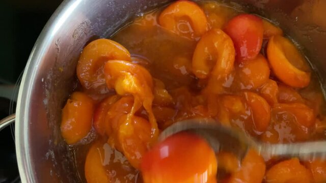Kochen von Aprikosenmarmelade. Umr&uuml;hren mit dem L&ouml;ffel im Topf.