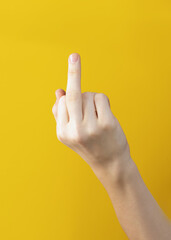 female hand shows middle finger on yellow background. gesture expresses demand to leave me alone. or expletive Fuck you