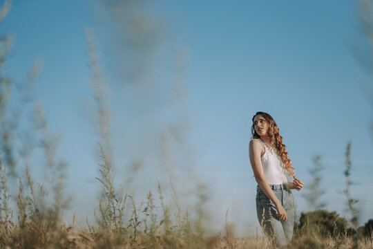 Spanish girl pulling on her blond locks in a wheat field on a sunny day under a clear ksy