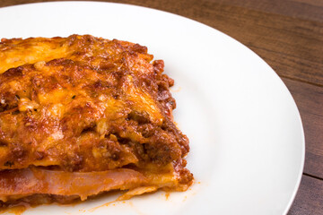 Lasagna in Bolognese sauce, made with ham cheese, tomato sauce and ground beef. Served on white plate.