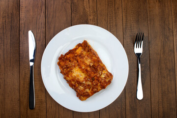 Tasty Lasagna in Bolognese sauce, made with ham cheese, tomato sauce and ground beef. Home made. Top view photography. Cutlery on the table. Pasta cuisine.