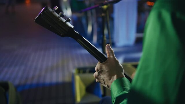 Hands of a guy playing a balalaika on stage in front of the audience. Twinkling lights all around