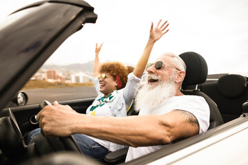 Happy senior couple having fun in convertible car during summer vacation - Focus on man face - obrazy, fototapety, plakaty