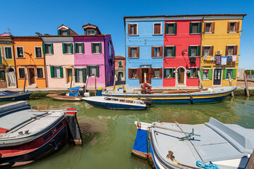 Naklejka na ściany i meble Burano island in the Venetian lagoon with multi colored houses (bright colors) and a canal with moored small boats in a sunny spring day. Venice, UNESCO world heritage site, Veneto, Italy, Europe.