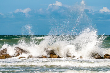 Riesige Welle trifft auf einen massiven Wellenbrecher aus Fels am Ostseestrand.