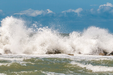 Riesige Welle trifft auf einen massiven Wellenbrecher aus Fels am Ostseestrand.
