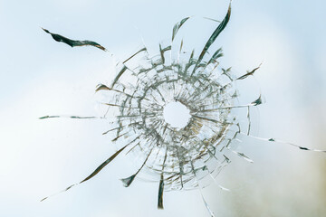 Bullet hole in dirty glass on the background of the sky with clouds, close-up