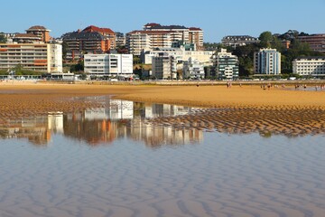 Fototapeta premium View of the beach with reflected buildings in a pool of sea water on a sunny spring June 2021 morning Sardinero Santander Cantabria Spain