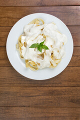 Tasty Tagliatelle pasta served with béchamel sauce and basil leaves. Pasta with white sauce. Top view photo. Vertical photograph with empty space below for texts.