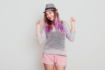 Portrait of young attractive girl with violet hair celebrating her success, raised arms, keeping...