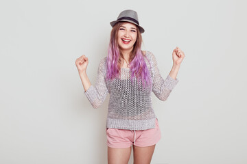 Portrait of happy female wearing hat, shirt and short, clenching fist with satisfied facial...