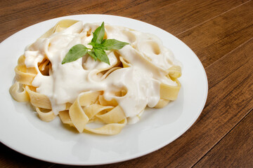 Tasty Tagliatelle pasta served with béchamel sauce and basil leaves. Pasta with white sauce.