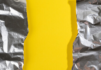 crumpled sheet of gray foil for packaging products with torn edges on a yellow background