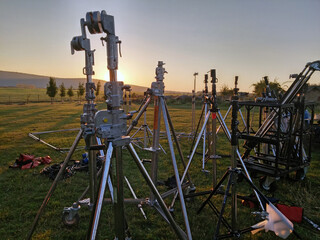 Lamp stands, tripods unloaded by film crew for filming, movie shooting in the dawn field in Hungary. - obrazy, fototapety, plakaty