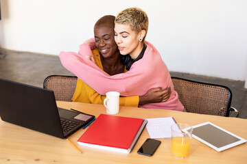 Lesbian couple hugging with laptop on table at home