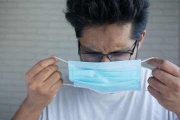 young asian man putting surgical face mask indoor 