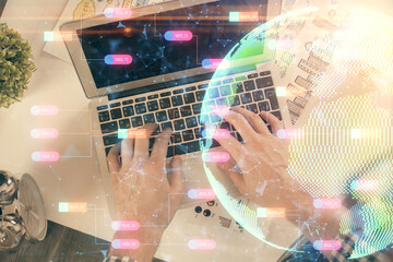 Multi exposure of man's hands typing over computer keyboard and world map hologram drawing. Top view. Technology concept.