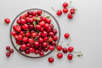 Sweet ripe cherries on plate placed on white table. Top view.