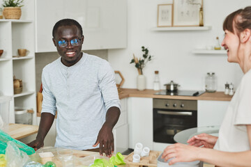 Young multiethnic couple cleaning up the house and throwing the rubbish in the kitchen