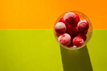 Cherry in ice crystals. Green orange background. Hard light. Top view. Copy space.