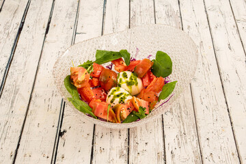 Glass bowl with chopped tomato salad, split burrata and spinach