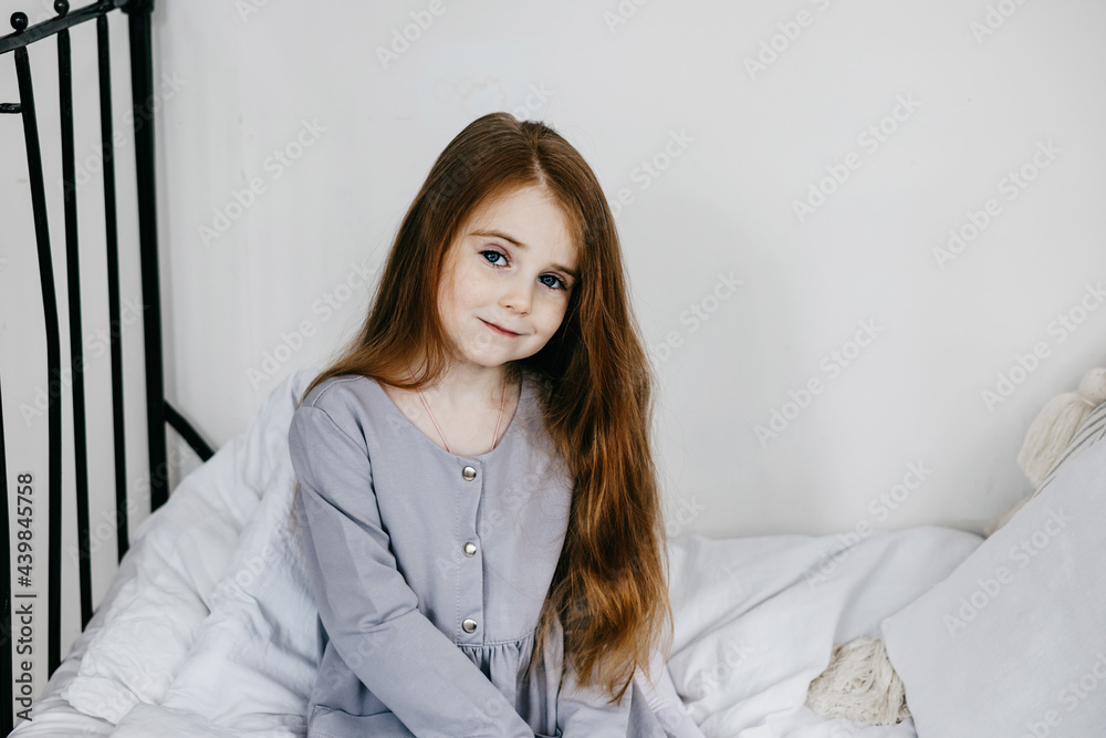 Wall mural little red haired girl sitting in a country house on a bed, summer vibes concept