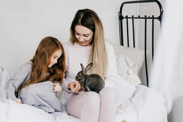 mom young woman and her little red haired girl daughter sitting in a country house with baby rabbit, summer vibes concept