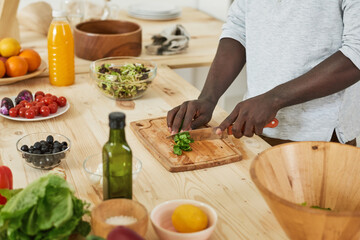 Obraz na płótnie Canvas Close-up of man cutting salad on cutting board at the table in the kitchen