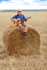 Naklejka na ściany i meble A man plays guitar on a haystack in a field