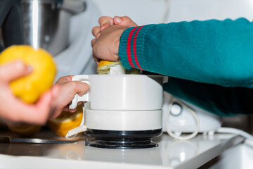 child hands make lemon juice in kitchen with school green uniform, white juice machine and white cook background